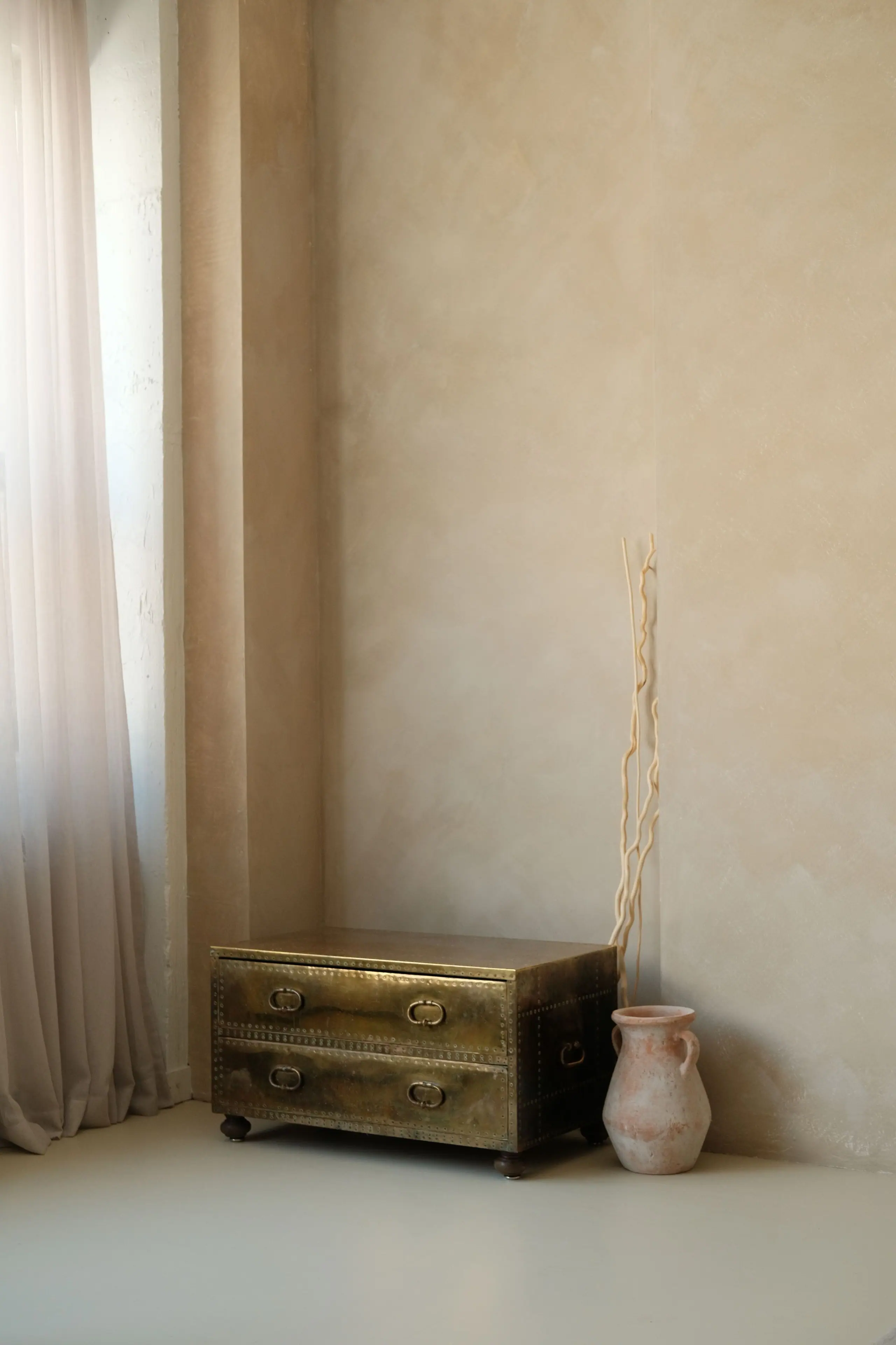 A brass-clad chest and clay vessel against a lime-washed wall