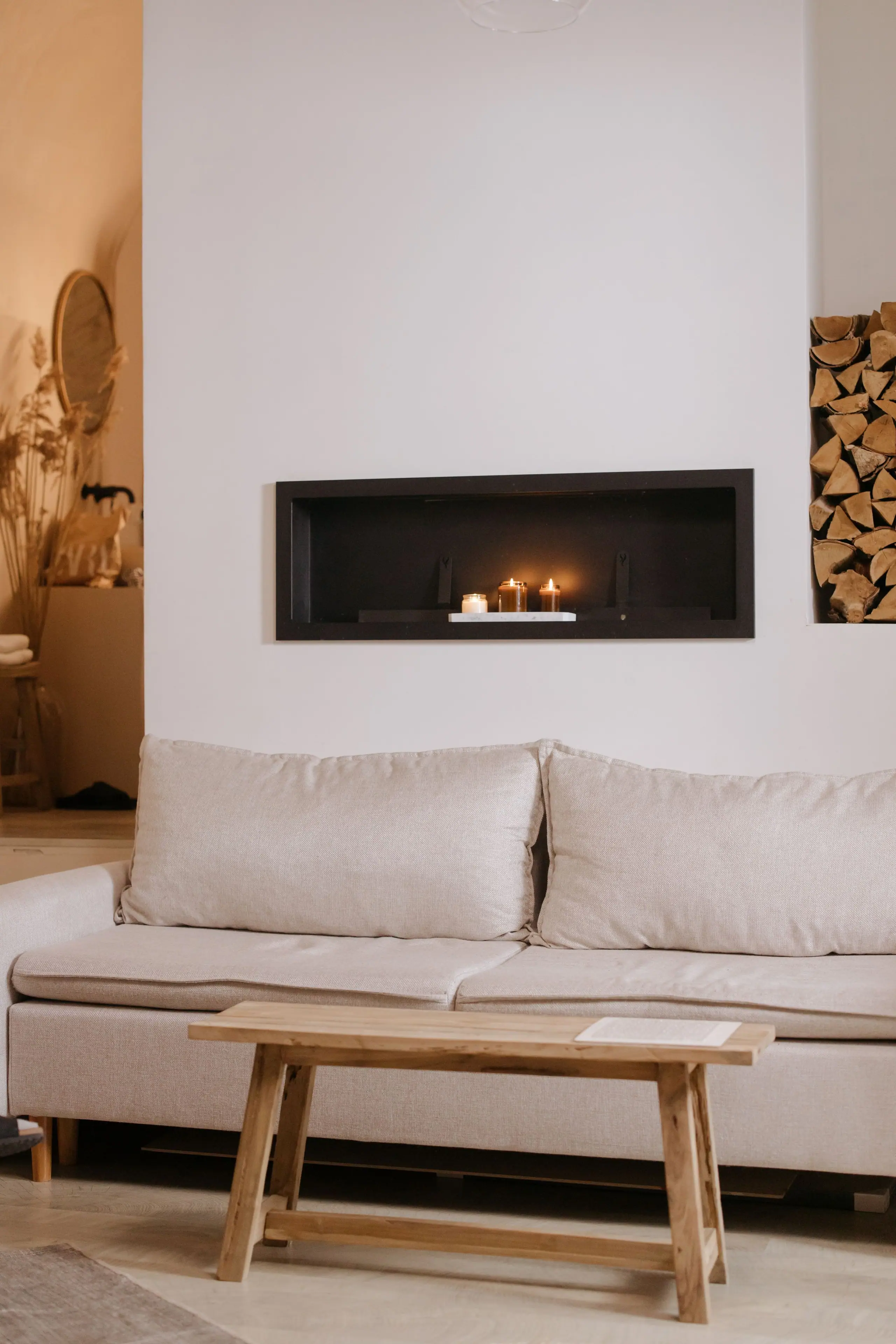 A pale living room with a linear fireplace set into a white wall, a linen sofa and an oak bench