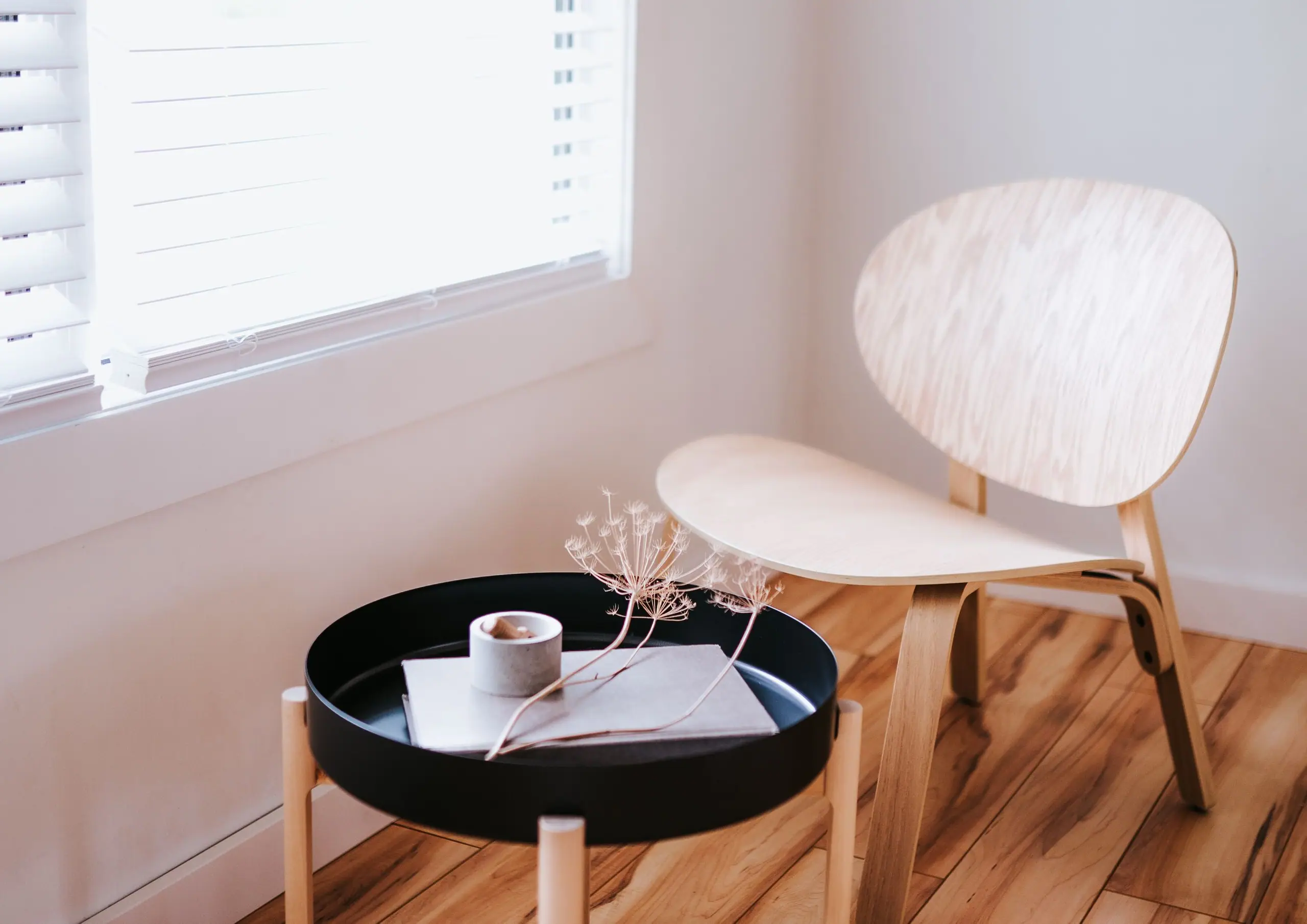 A pale plywood lounge chair and black tray table in soft window light