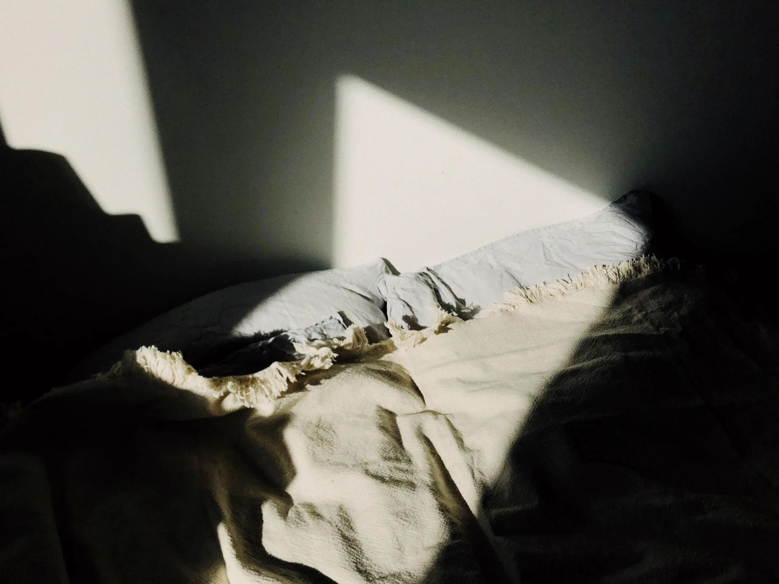 Afternoon sun falling across linen bedding in a dim bedroom