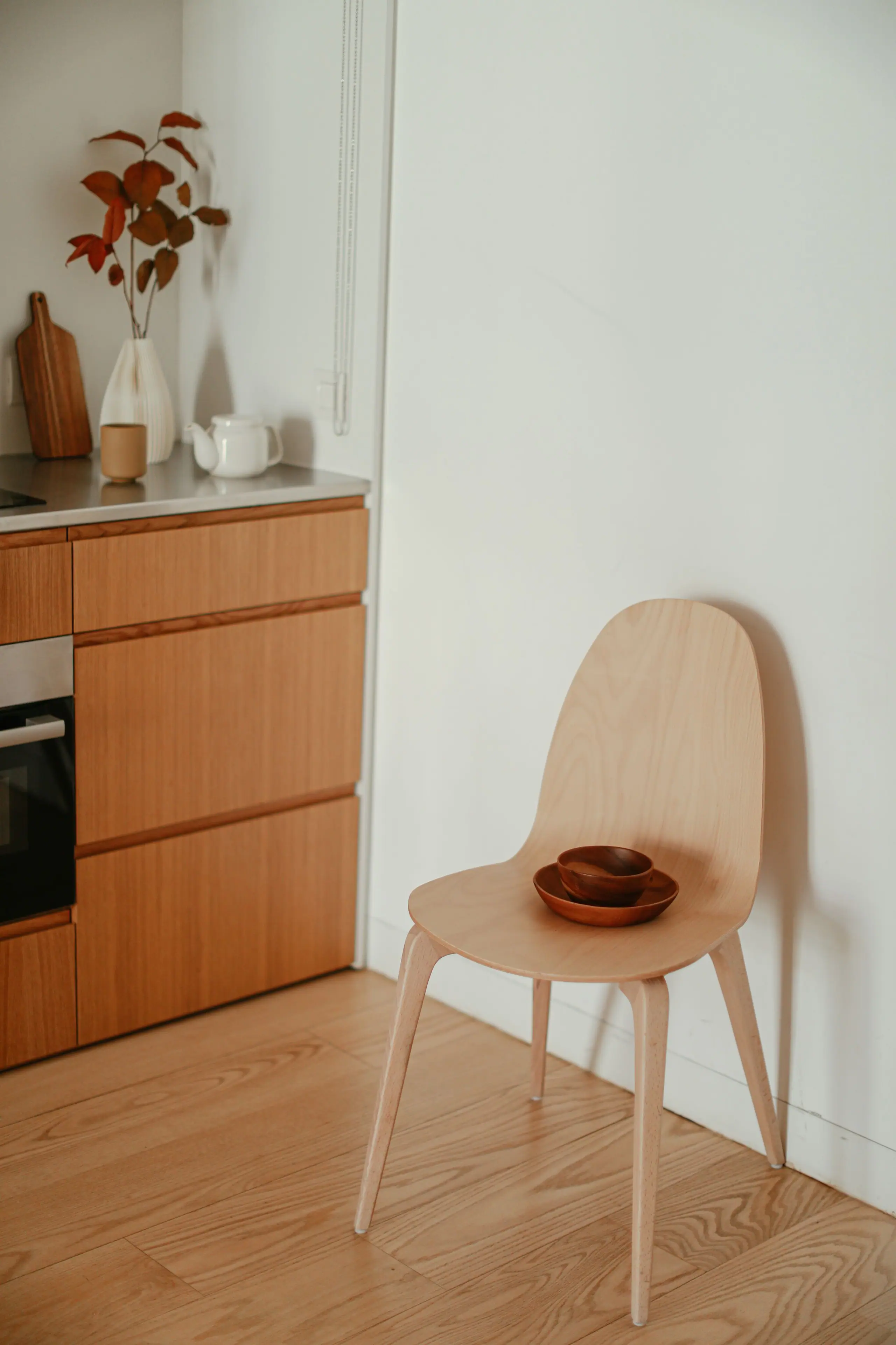 A simple oak chair against a white wall beside the kitchen run