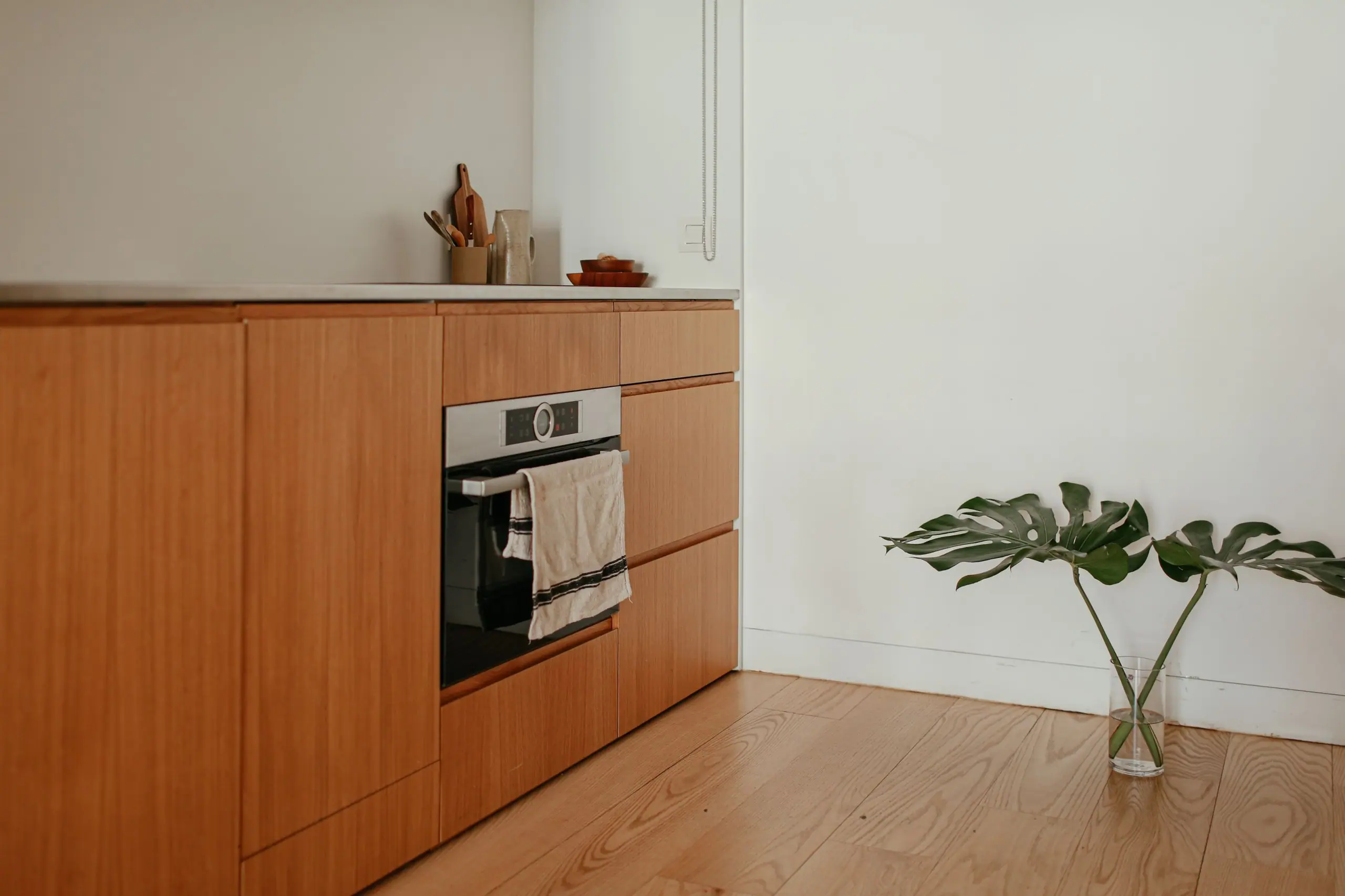 Oak kitchen cabinetry with an integrated oven and a single stem of monstera in a glass vase