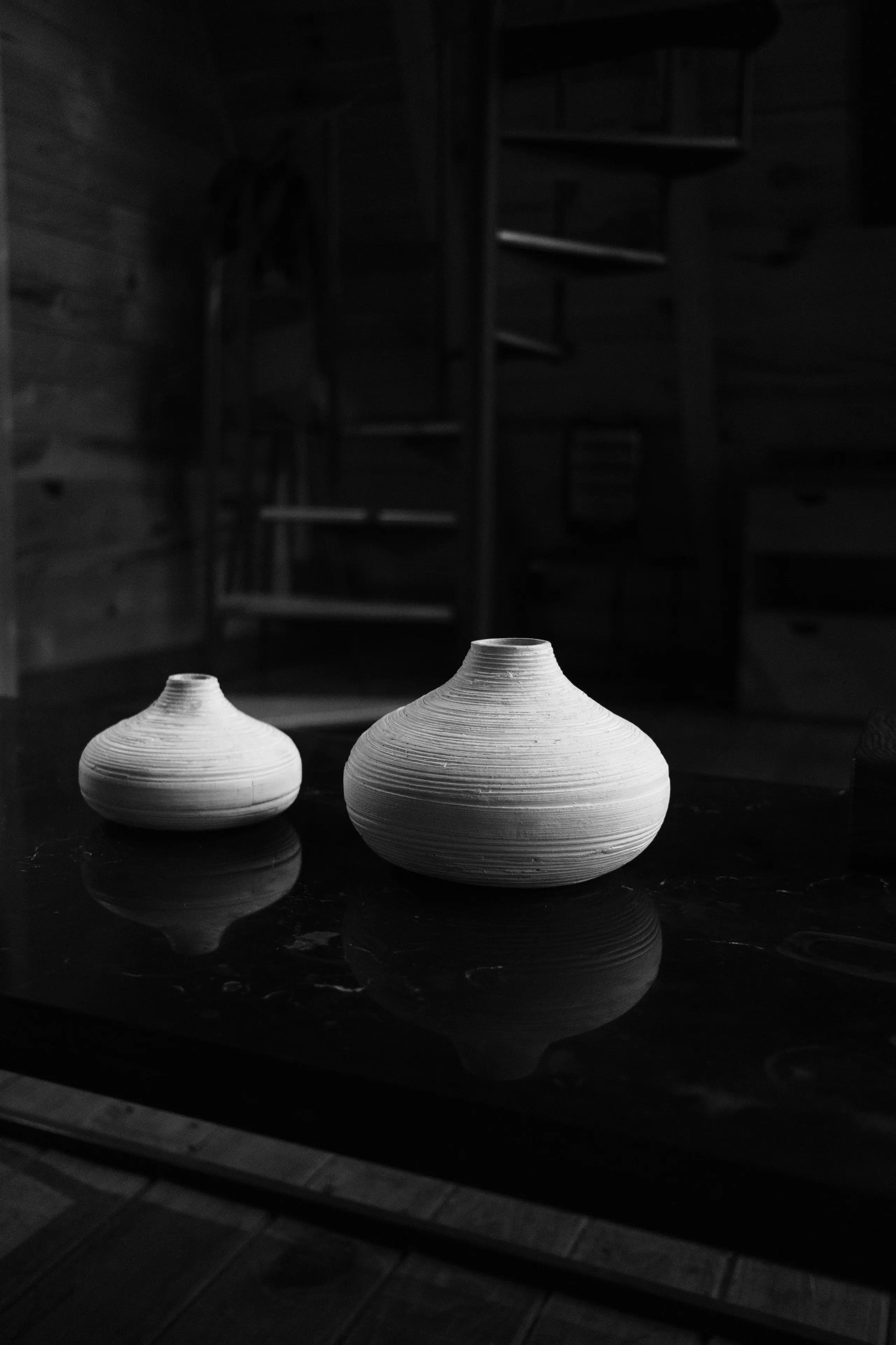 Two pale ceramic vessels on a dark polished surface