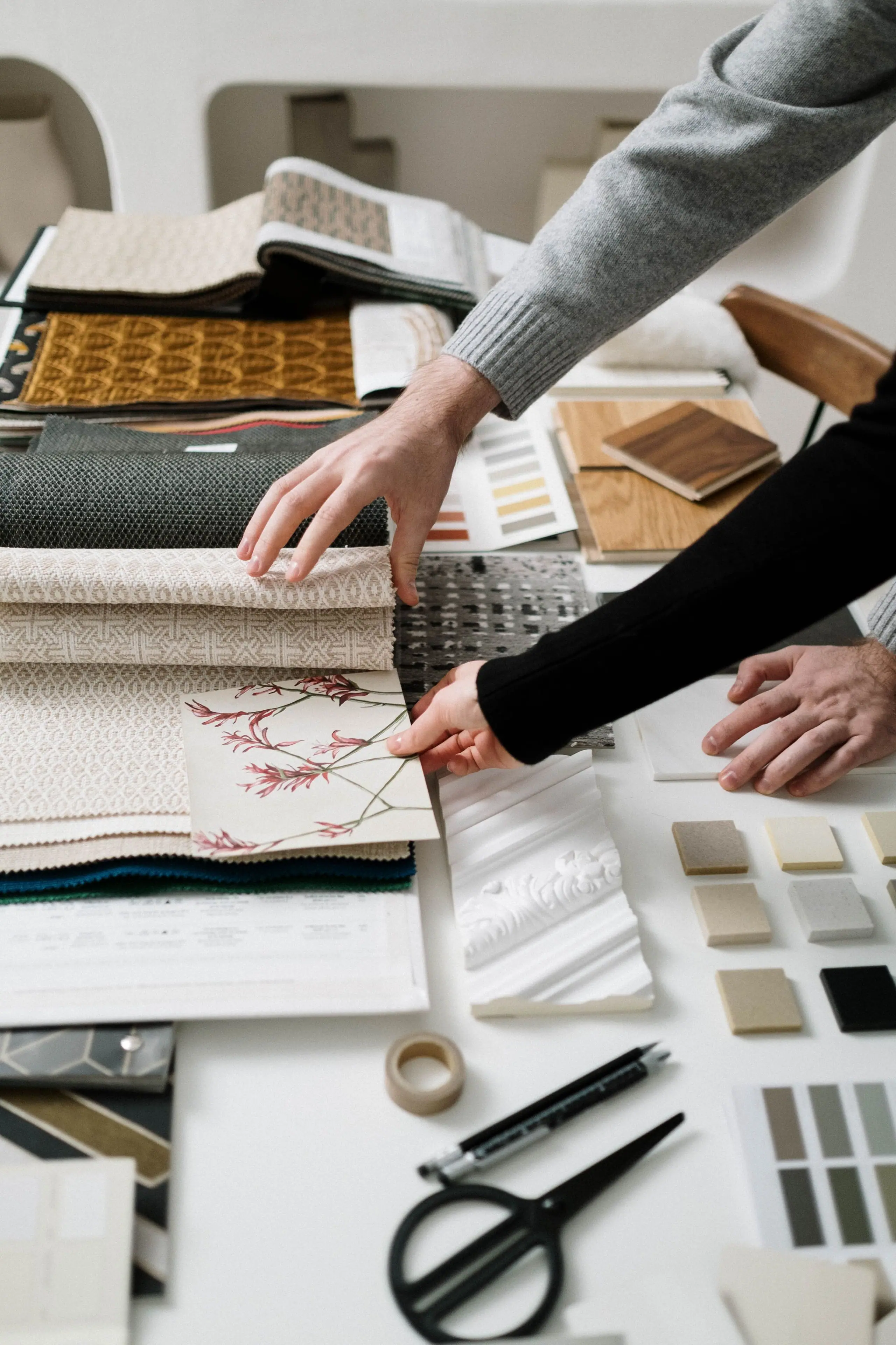 Hands sorting fabric, timber and stone samples across a white table
