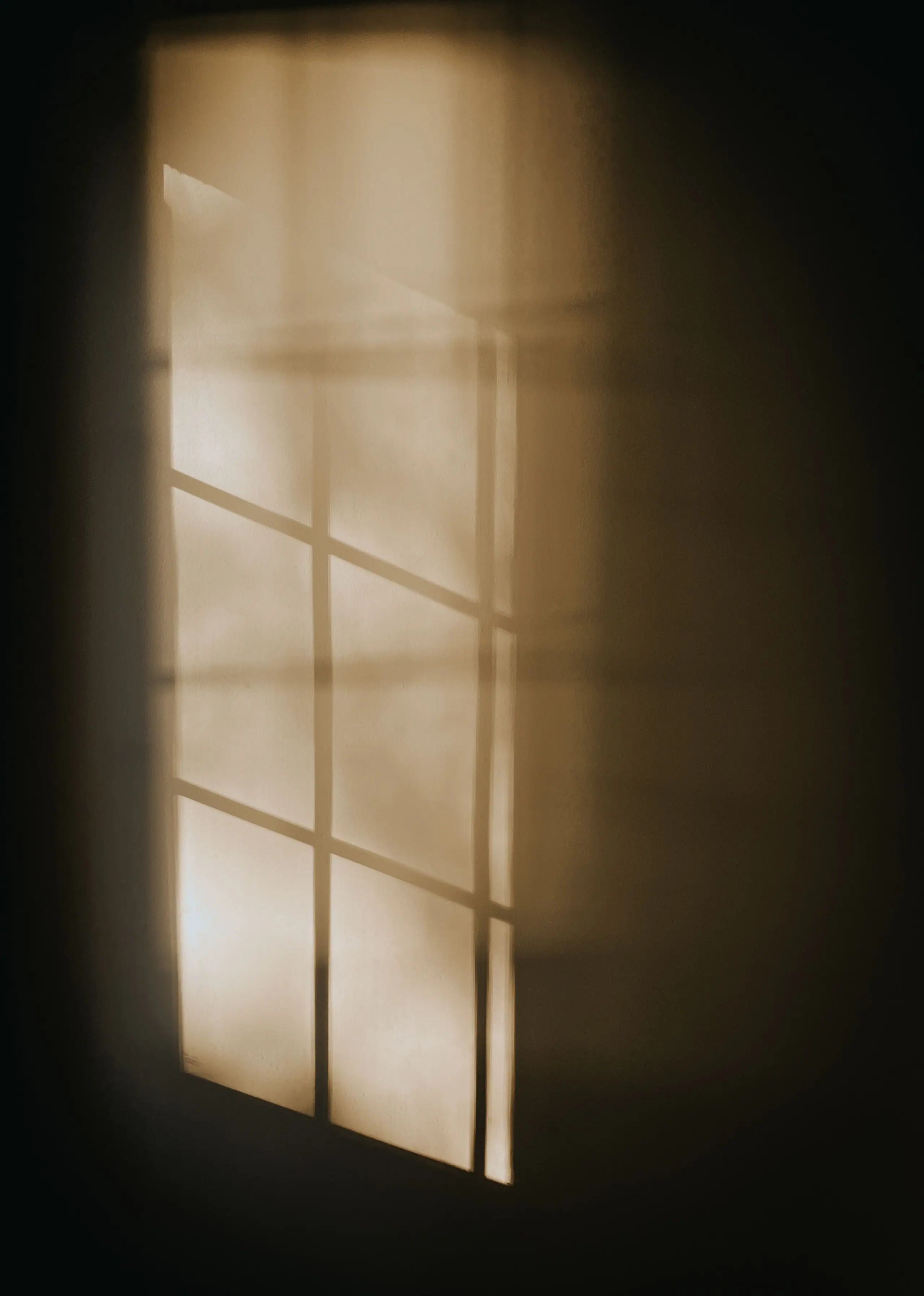 The shadow of a window frame falling across a warm plaster wall