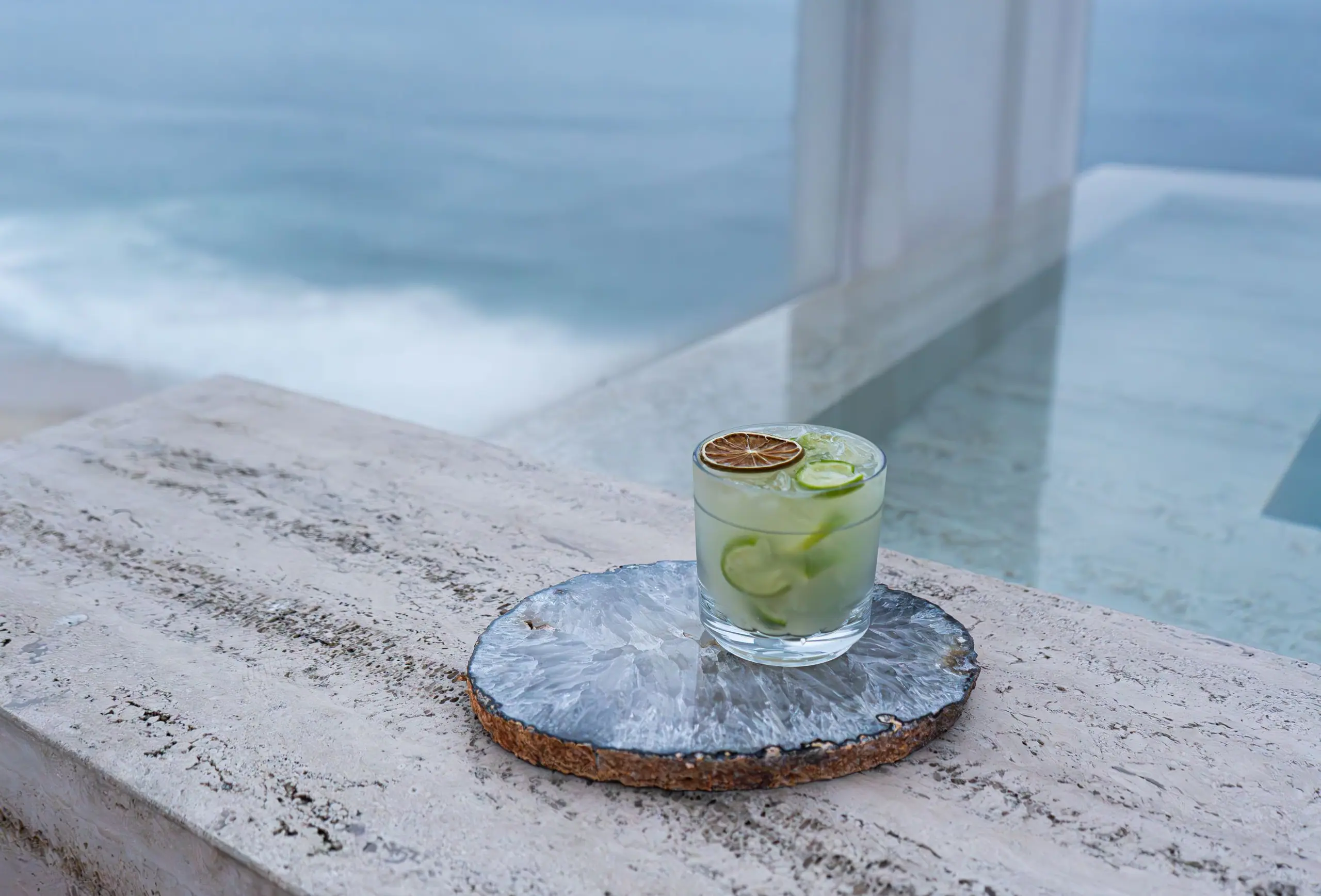 A honed travertine ledge beside a pool, with a glass resting on a stone coaster