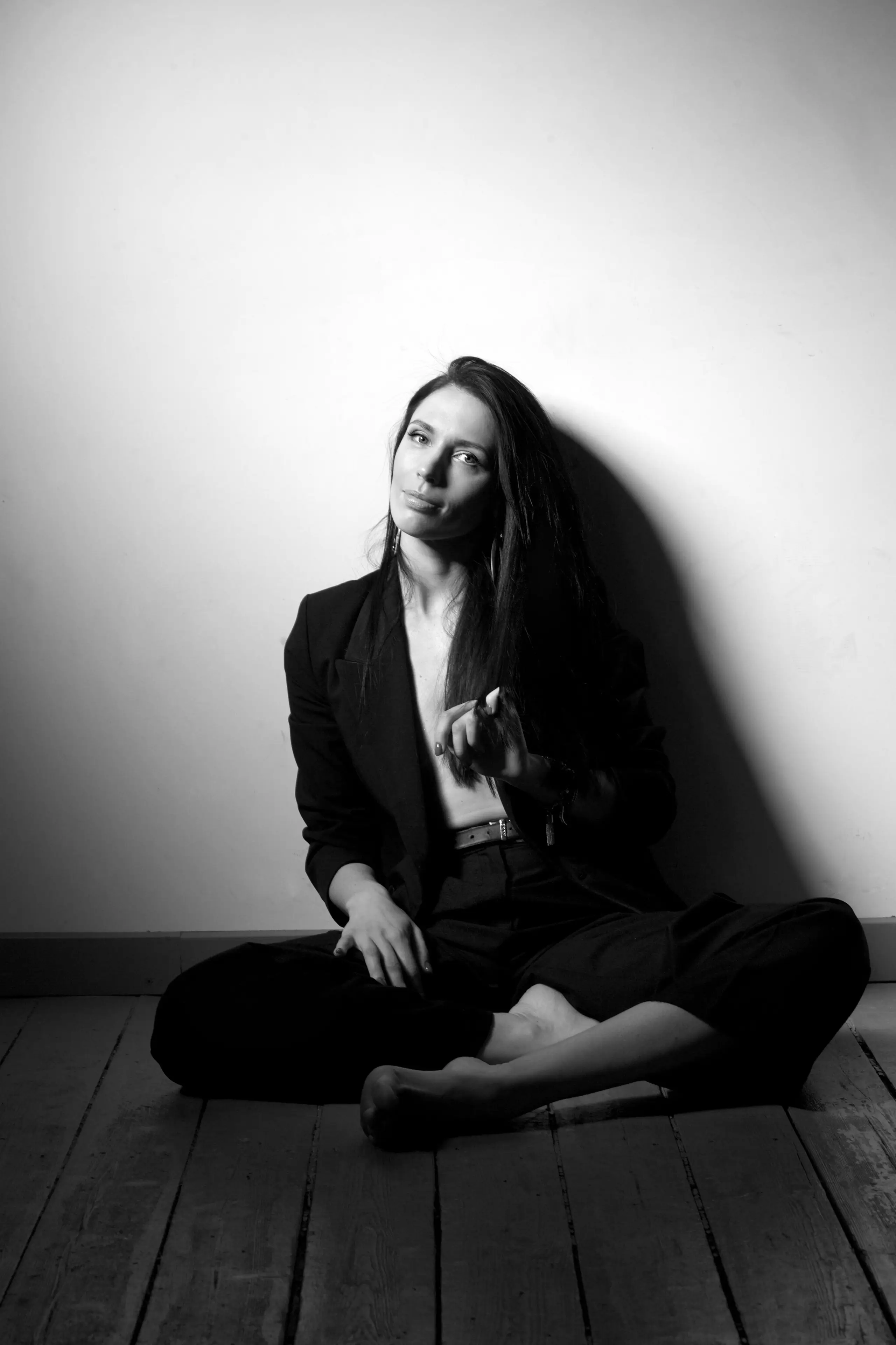 Black and white portrait of Claire Harrison sitting on a timber floor against a white wall