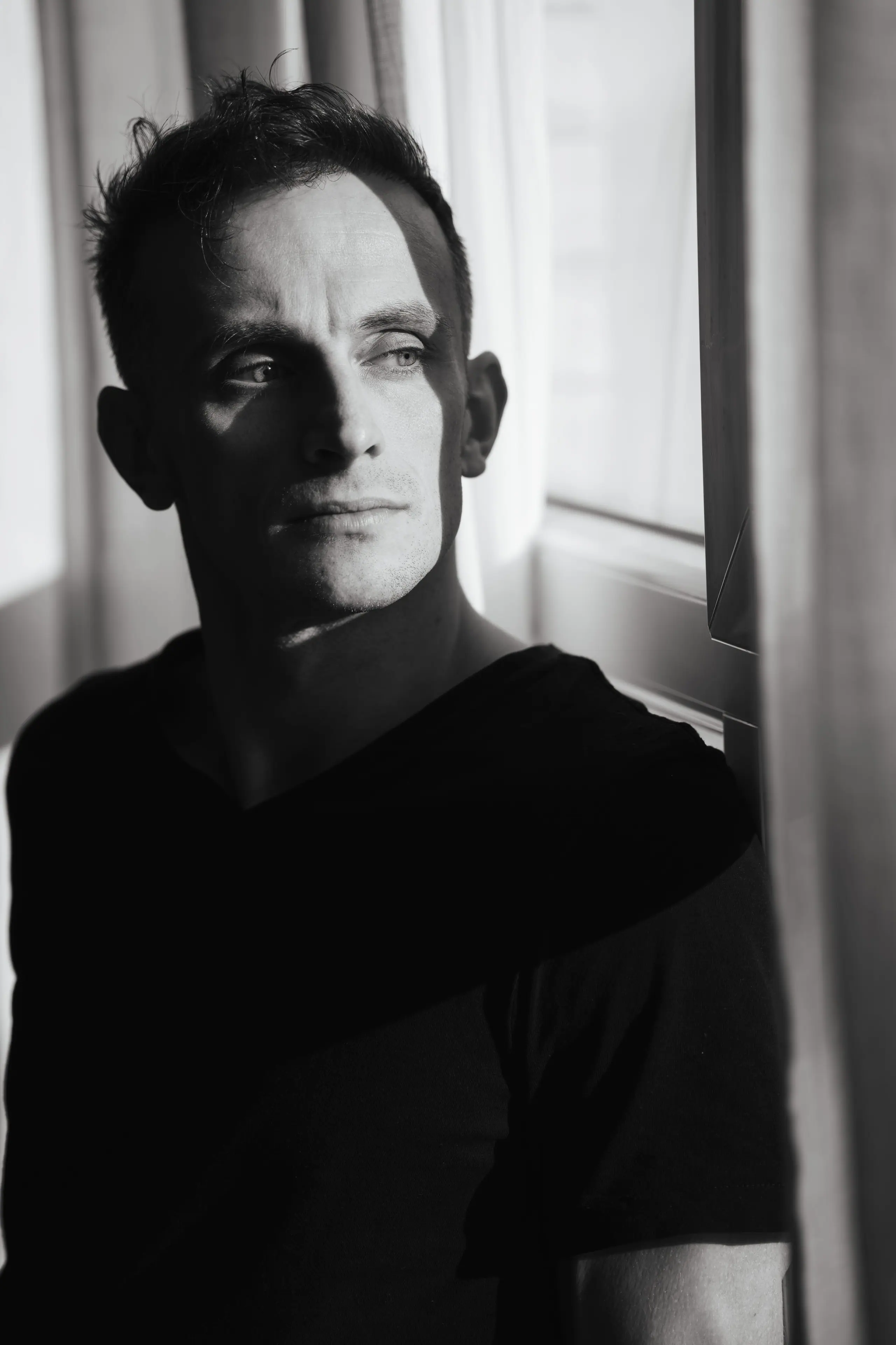 Black and white portrait of Ethan Vale by a window, half in shadow