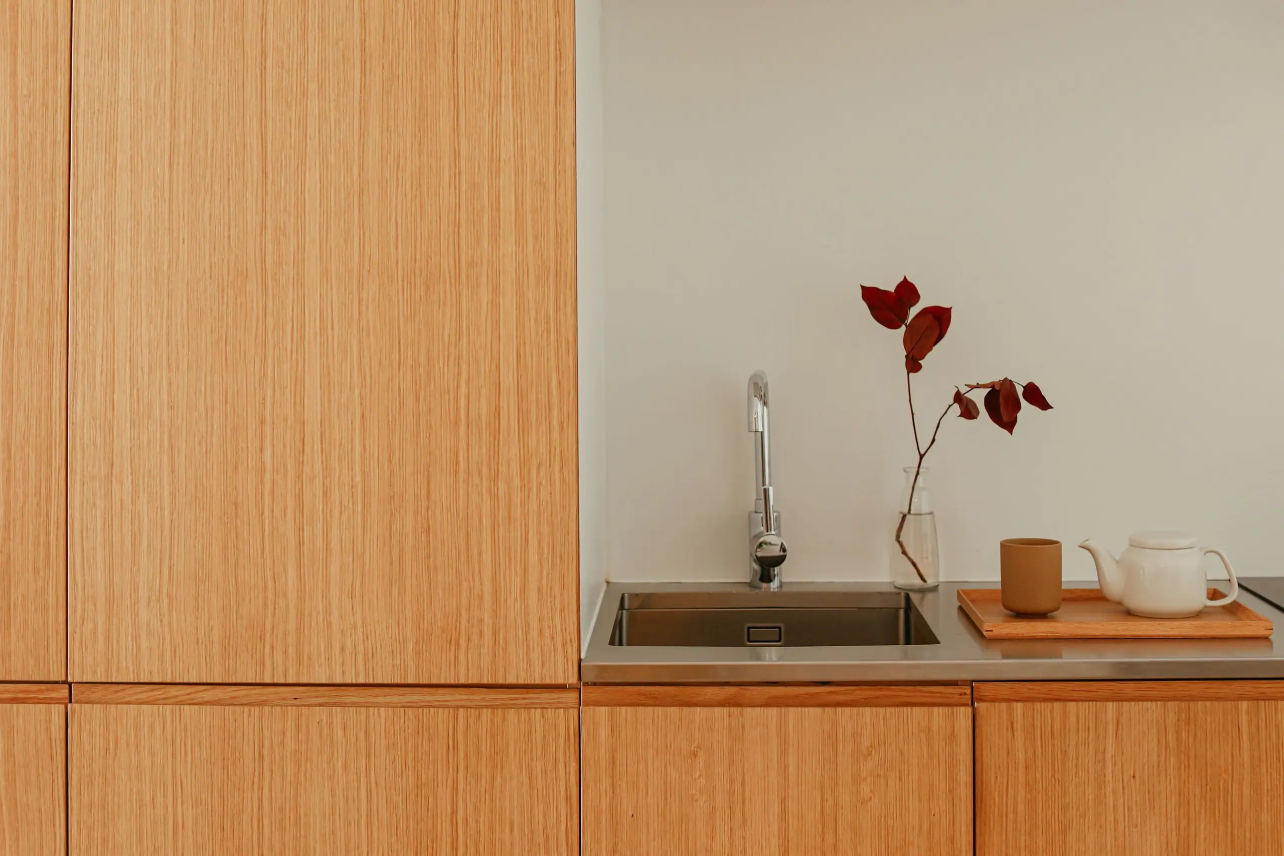 Oiled oak kitchen joinery with a steel sink and a single red stem in a bottle