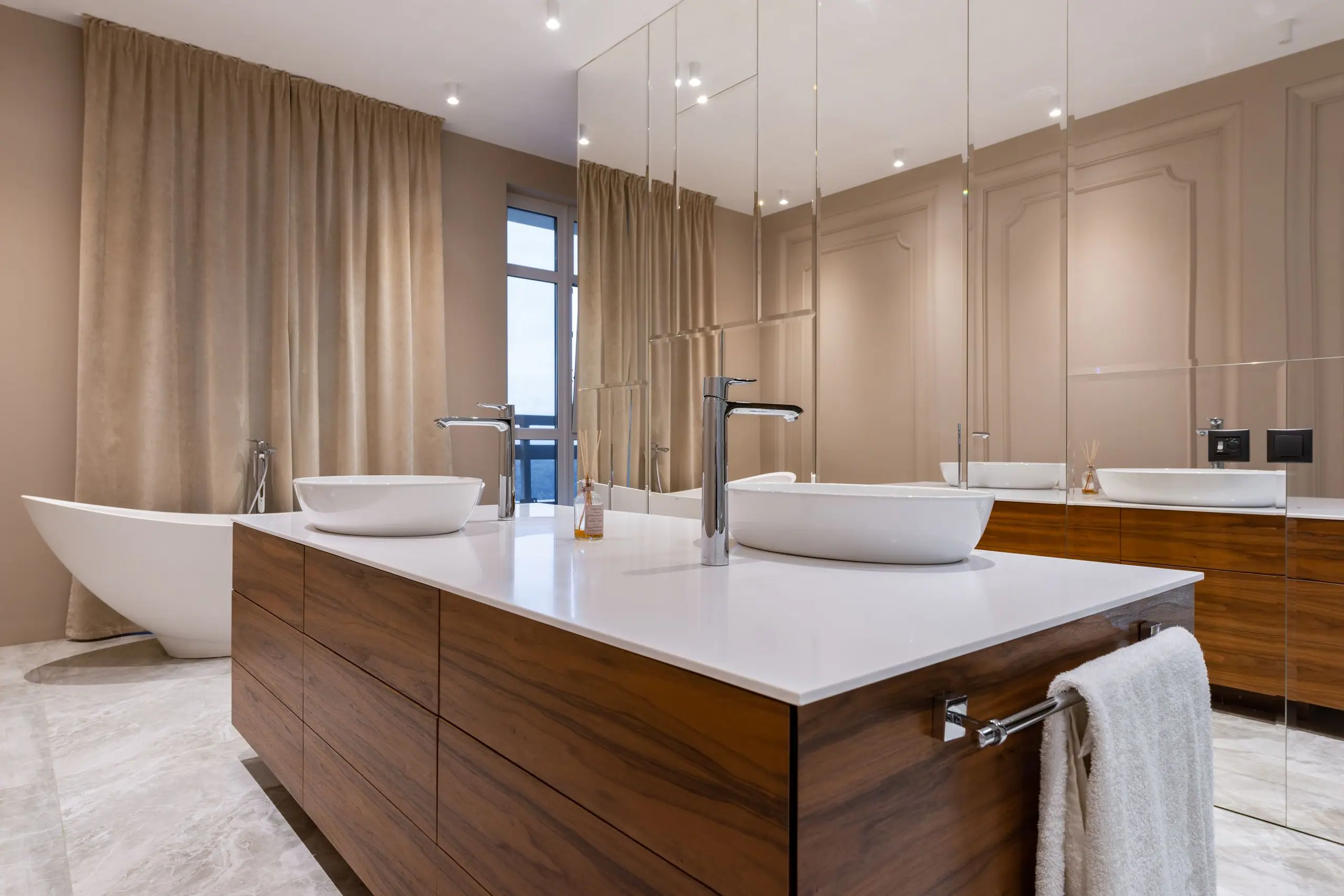 A walnut vanity island with twin stone basins and a freestanding bath beyond