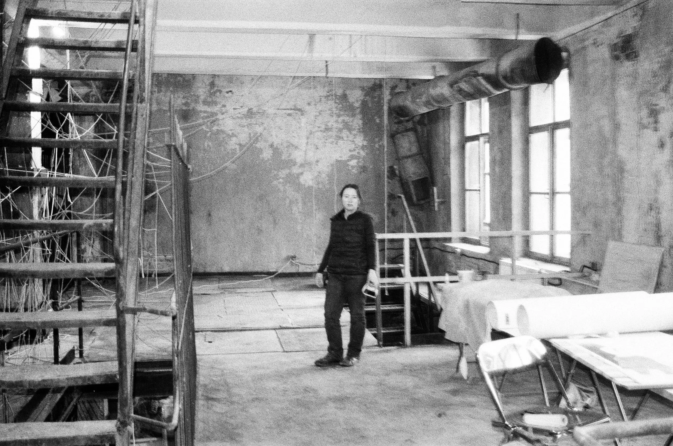 Black and white photograph of an architect standing in a stripped-back mill interior during a site visit
